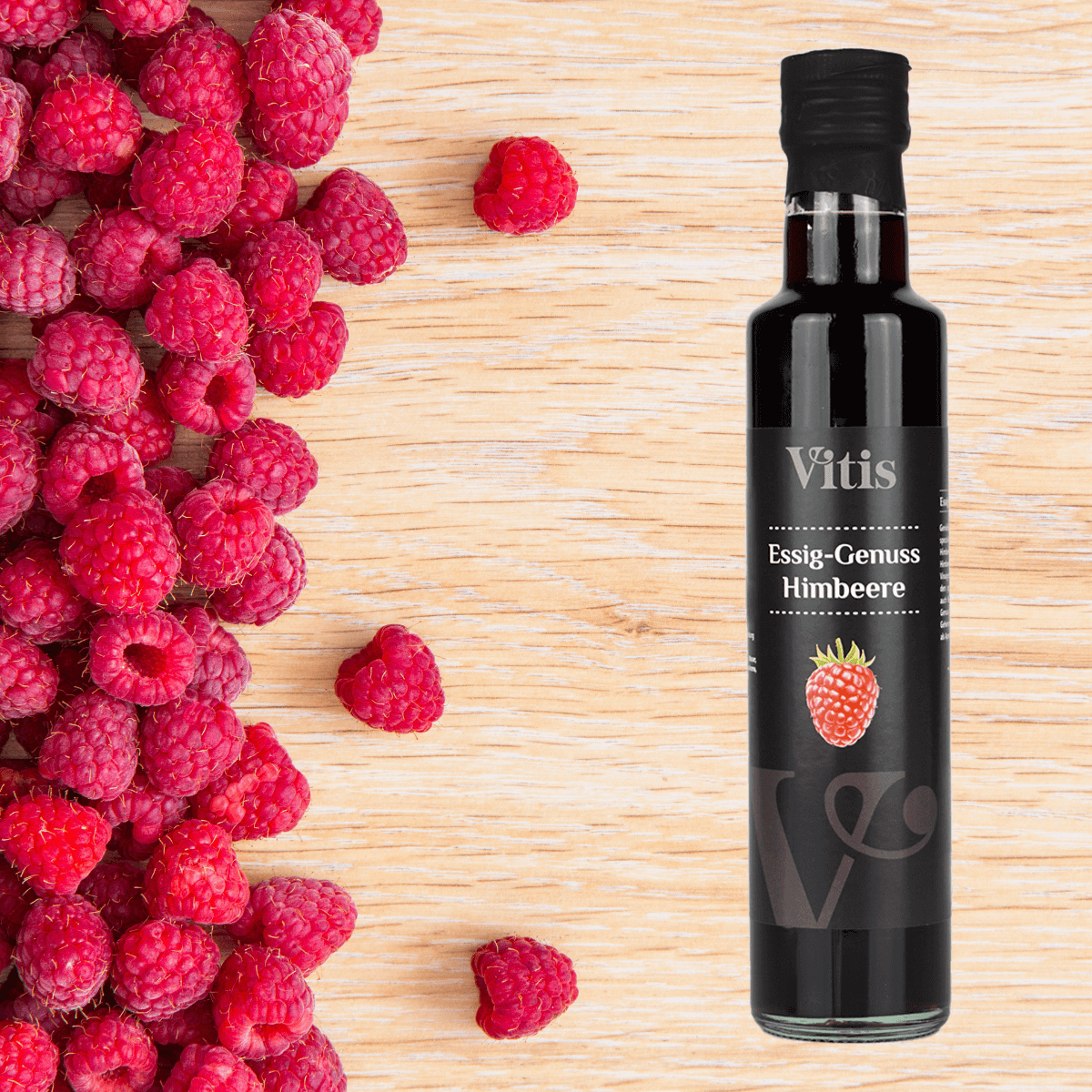 Eine Flasche Himbeeressig von Vitis auf einem Hintergrund aus Holz. Daneben sind Himbeeren zu sehen.
