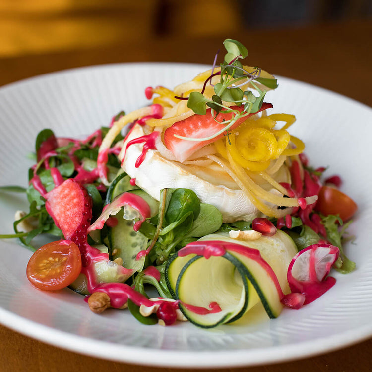 Ein Balttsalat mit Tomaten, Gurken, Erdbeeren und einem Stück Camembert auf dem Salat