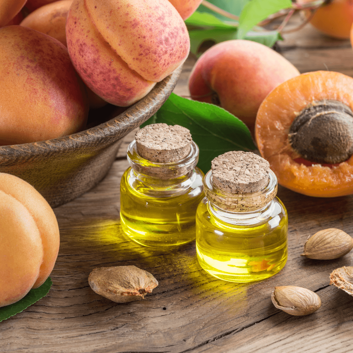 Ein Bild mit zwei kleinen Fläschchen Aprikosenkernöl. Im Hintergrund sind reife Aprikosen zu sehen. 