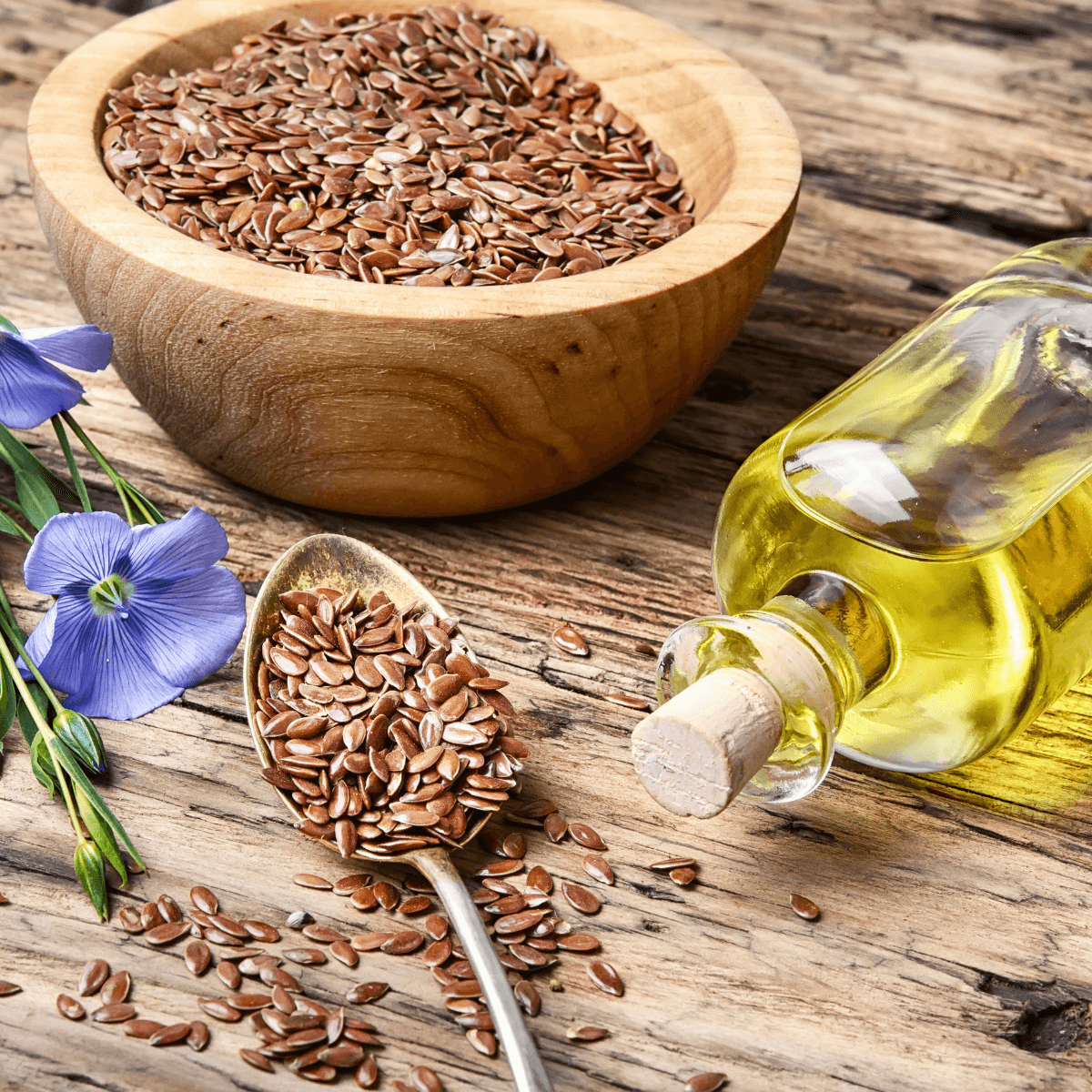 Leinsamen in einer Holzschale neben einer Flasche Leinöl auf einem Holztisch.