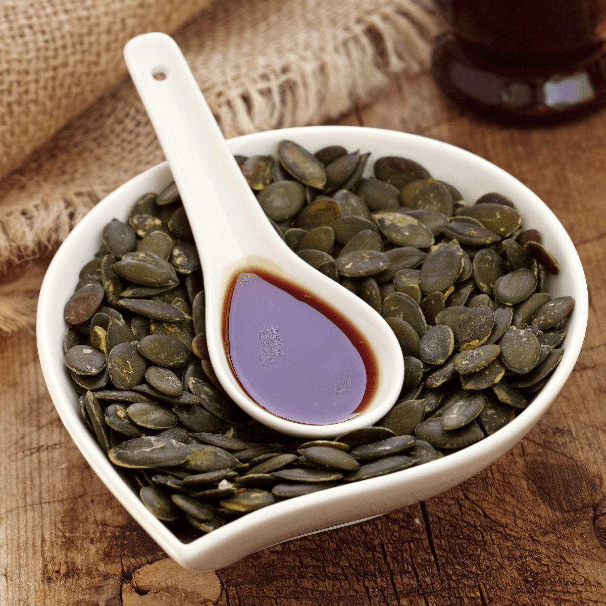 Eine weiße Schale geröstete Kürbiskerne auf dem ein weißer Löffel Kürbiskernöl liegt.