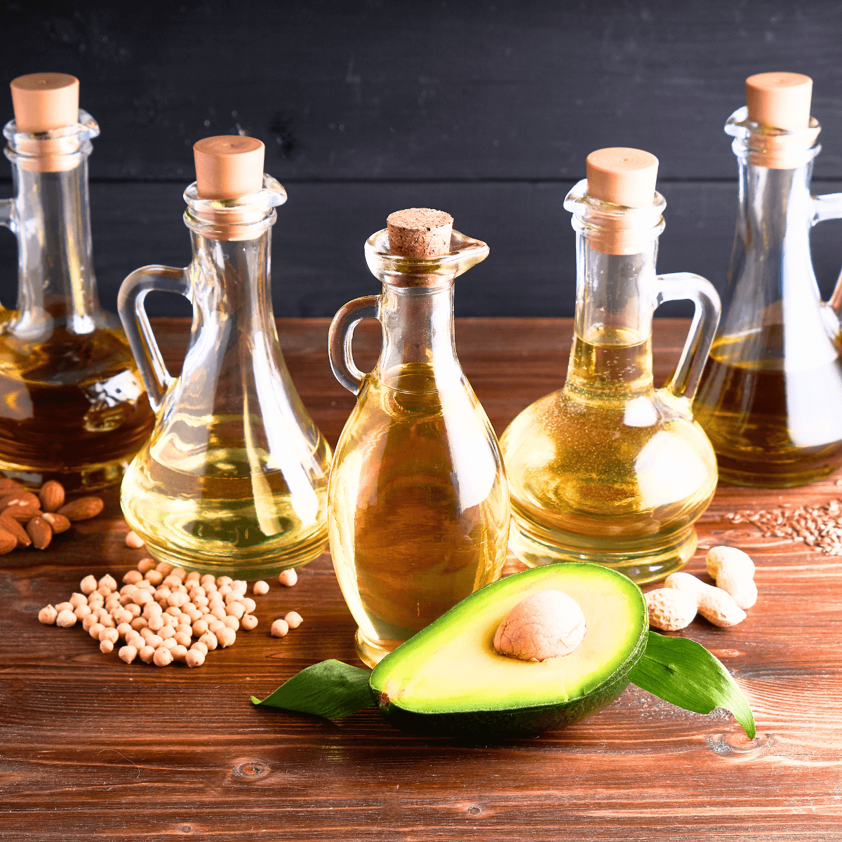 Verschiedene Speiseöle stehen in unterschiedlichen Flaschen auf einem Holztisch.