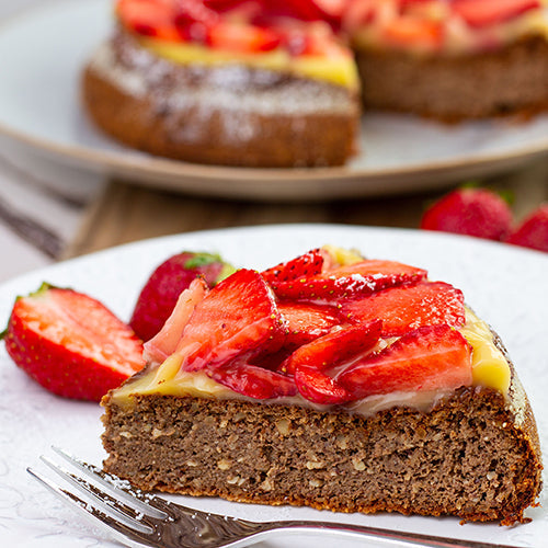 Ein Stück Erdbeerkuchen mit dunklem Teig und Vanillepuddingschicht auf einem Teller mit Kuchengabel.