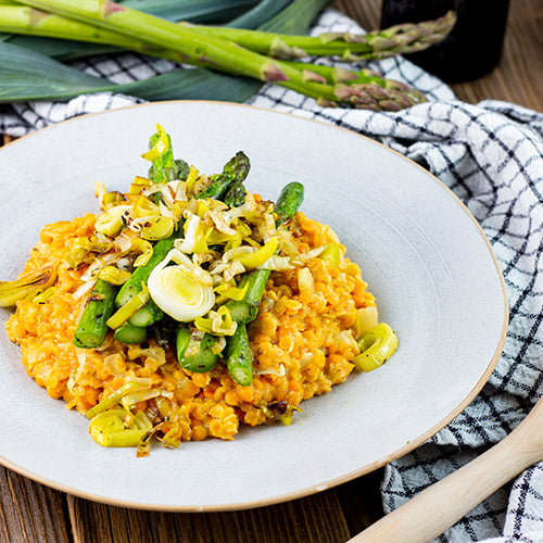 Linsenrisotto mit grünem Spargel auf einem weißen Teller angerichtet.