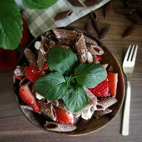 Eine Salatschale mit Traubenkernnudeln und Erdbeeren gefüllt.
