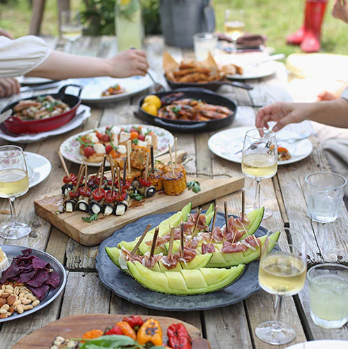 Ein Holztisch mit Fingerfood und Getränken, an dem Menschen sitzen und essen.