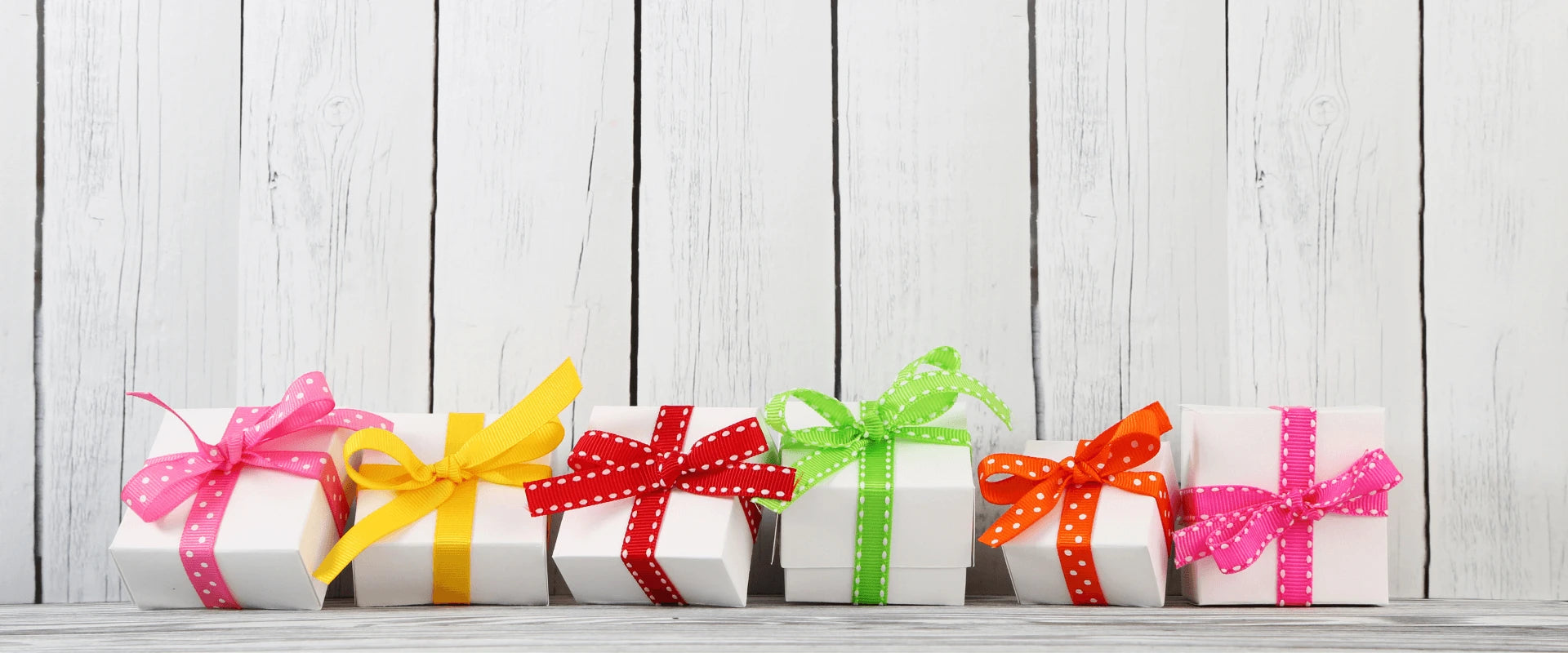 Kleine Geschenke mit bunten Schleifen sind gegen einen weißen Zaun gelehnt.