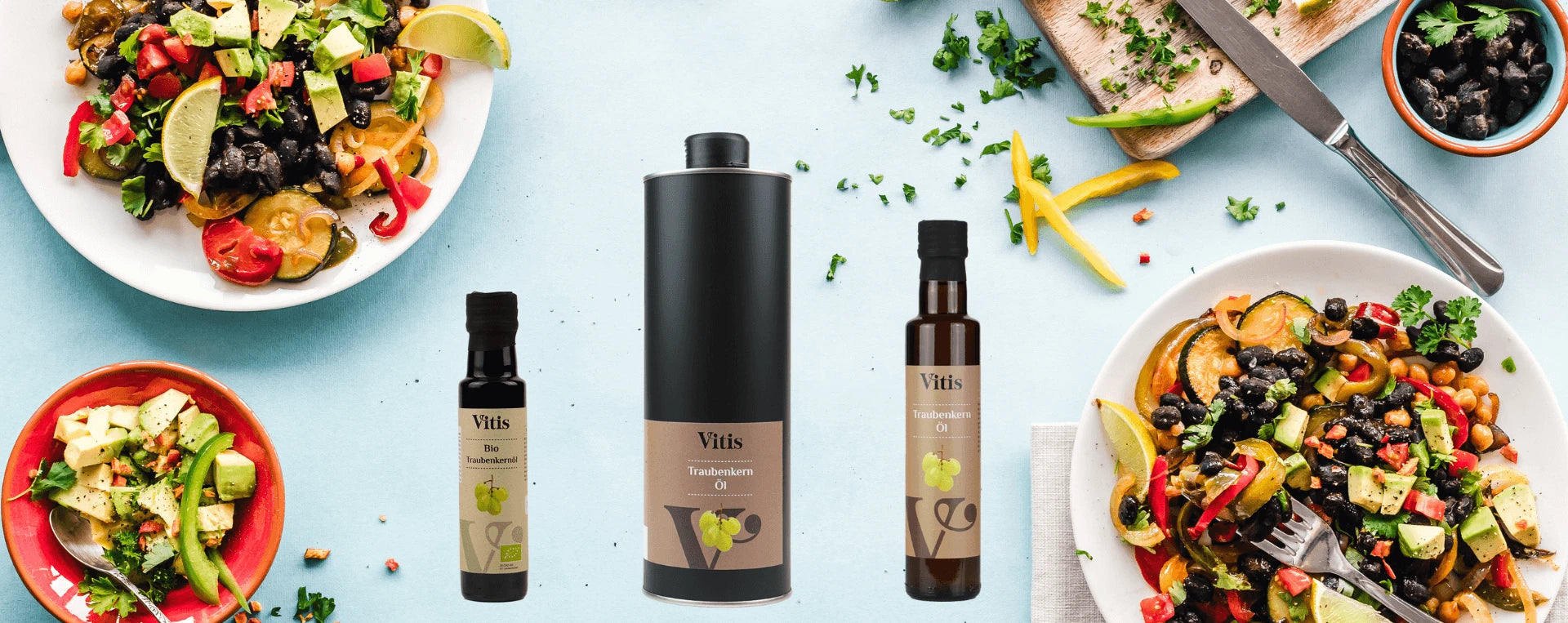 Traubenkernöl Flaschen von Vitis in verschiedenen Größen. Im Hintergrund sind Teller mit verschiedenen bunten Salaten zu sehen.