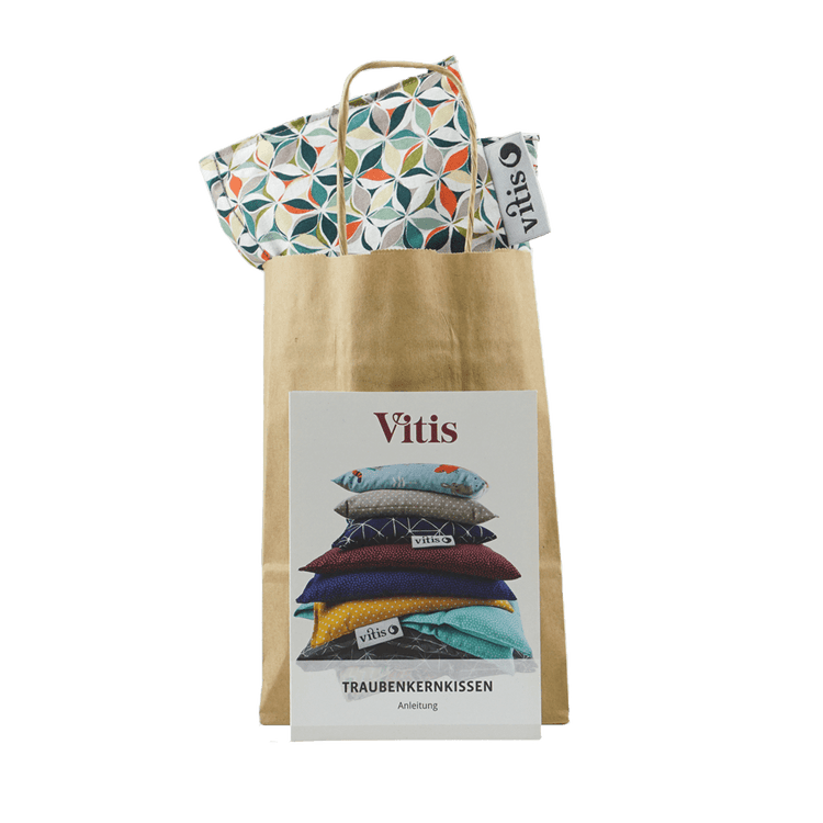 Eine Papiertüte mit dem Multicolor Traubenkernkissen der Firma Vitis Traubenkern GmbH. Dazu im Vordergrung eine Anleitung für die Verwendung des Traubenkernkissens.