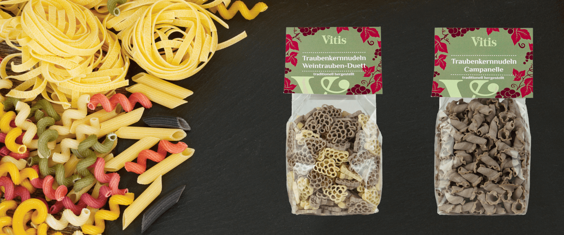 Die Traubenkernnudeln Campanelle und Weintrauben Duett auf dunklem Hintergrund. Auf der linken Seite ist Pasta in verschiedenen Formen und Farben zu sehen.