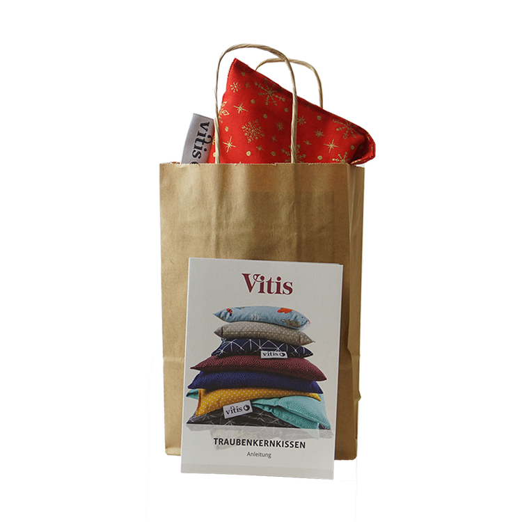 Eine Papiertüte mit einem kleinen weihnachtlichen Traubenkernkissen von Vitis24 mit einer Anleitung zur Nutzung des Traubenkernkissens im Vordergrund.